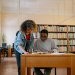 Two university students studying together in a library, focusing on textbooks and learning.