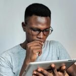 Young man wearing glasses engrossed in using a tablet device indoors.
